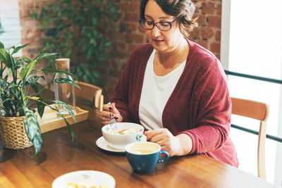 Adult brunette woman in glasses in casual clothing plus size body positive having lunch at cafe