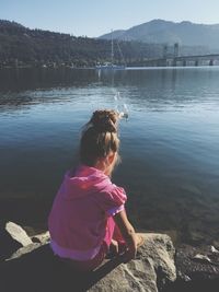 Rear view of man sitting on bench in front of lake