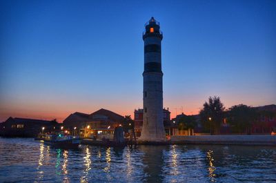 View of lighthouse by building against sky during sunset