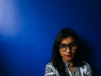 Close-up portrait of teenage girl wearing eyeglasses against blue wall