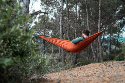 Man sitting on hammock against trees