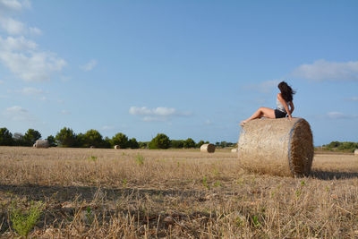 Woman sitting on field against sky