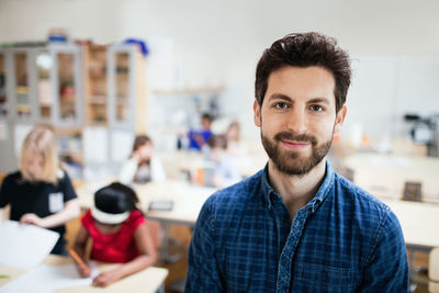 Portrait of confident teacher with students studying in background