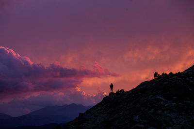 Silhouette of distant anonymous explorer standing alone on hill slope against cloudy sunset sky in pyrenees mountains