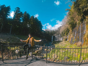 Man sitting by railing against trees