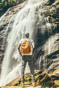 Man standing on a stone looking at waterfall during the day