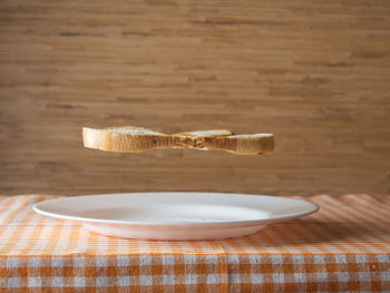 Close-up view to levitation of bread over empty dish on table at home. horizontal frame.