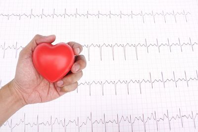 Cropped hand holding heart shape against pulse trace