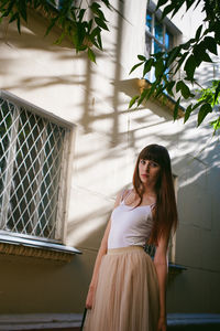 Portrait of young woman standing against building