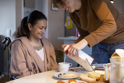 Female caregiver pouring milk in cup for woman with disability at home