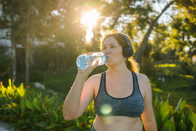 Young woman drinking water while standing outdoors