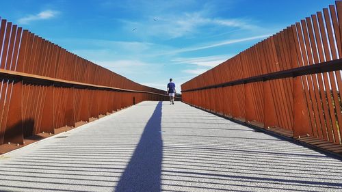 Rear view of man walking on walkway against sky