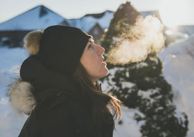 Side view of woman exhaling breath vapor during winter
