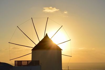 Silhouette traditional windmill by sea against sky during sunset