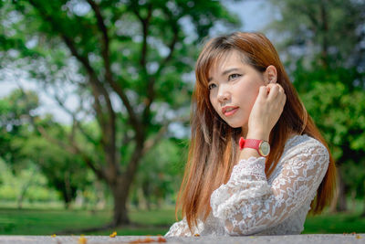 Portrait of young woman looking away against trees