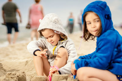 Siblings making sandcastle while crouching at beach