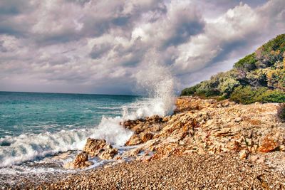 Waves splashing on rocks at shore against sky