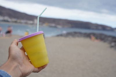 Midsection of person holding yellow umbrella on beach