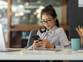 Smiling businesswoman using mobile phone at office