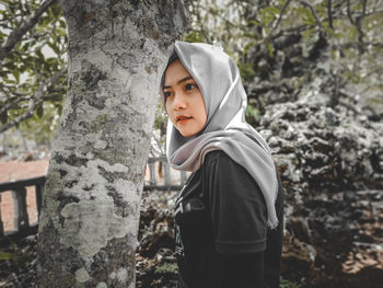 Portrait of teenage girl standing against tree trunk