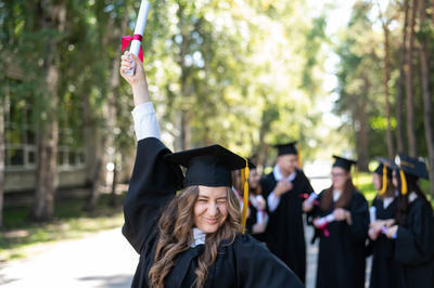 Portrait of woman wearing graduation gown standing in park