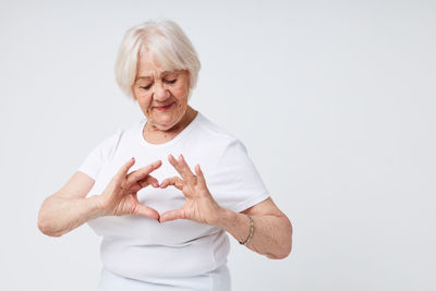 Senior woman making heart shape against white background