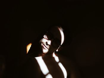 Shirtless young man wearing sunglasses standing in darkroom