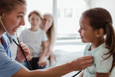 Female pediatrician listening to girl's heartbeat through stethoscope at clinic
