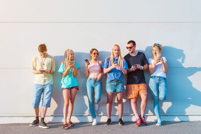 Group of friends using mobile phone while standing against the wall