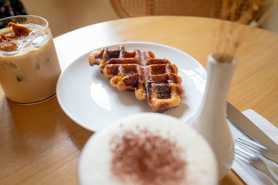 Two cups of coffee, honey latte and eispanner americano served with waffle on plate.