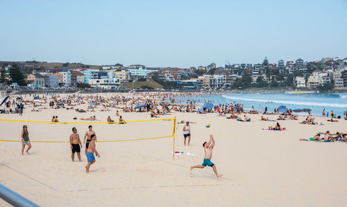 People playing on beach against clear blue sky