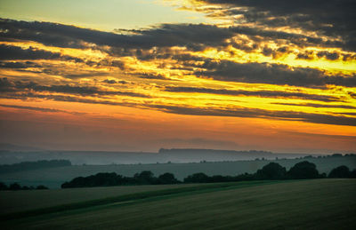 Scenic view of field against dramatic sky during sunset