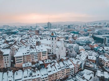 Aerial view of snow covered townscape against sky at sunset