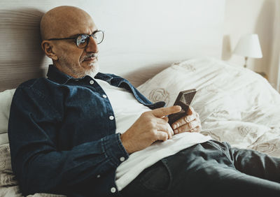 Man using mobile phone while sitting on bed at home