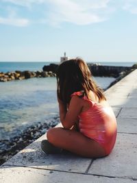 Woman sitting on shore at beach against sky