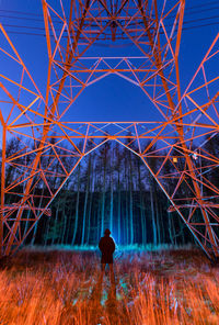 Man standing on field against electricity pylon at night