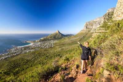 Rear view of woman pointing while standing on mountain by sea against clear sky