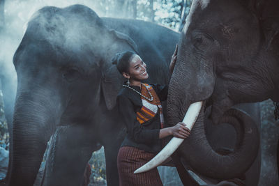 Smiling woman standing with elephant in forest