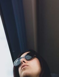 Low angle view of young woman wearing sunglasses looking through window