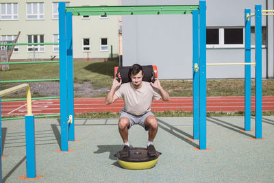 Man with a 10kg dumbbell with water on his shoulders does a squat on a balance beam