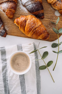 Flat lay of cup of cappuccino with kitchen towel and eucalyptus branch, brown croissants