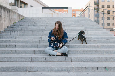 Young adult woman sit looking her phone and next to her dog after walk