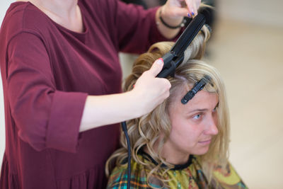 Midsection of female hairdresser using equipment on blond bride at salon