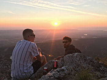 People on rock against sky during sunset