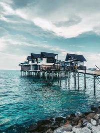 Stilt house on sea by building against sky