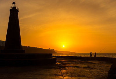 Silhouette of lighthouse at beach during sunset