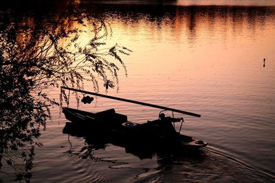 Silhouette boat moored on lake against sky during sunset