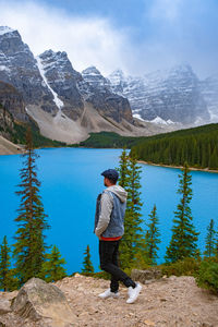 Rear view of man standing by lake against mountain