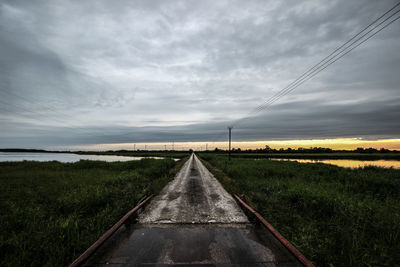 Road passing through field against cloudy sky