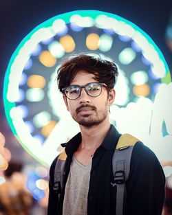 Portrait of confident young man at illuminated amusement park